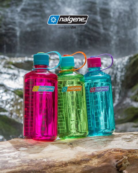 Tres coloridas botellas de agua Nalgene (rosa, verde y azul) están sobre un tronco de árbol frente a una cascada. Cada botella tiene una tapa de rosca y una correa de transporte. Encima de ellas se muestra el logotipo de Nalgene con la leyenda "Hecho en EE. UU.".