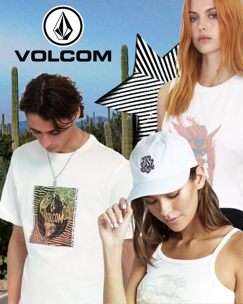 Tres modelos con ropa de Volcom posan frente a un paisaje desértico con cactus. El modelo masculino lleva una camiseta blanca con gráficos, la modelo femenina con pelo naranja lleva un top blanco y la otra modelo femenina lleva una gorra y una camiseta de tirantes blanca. Logotipo de Volcom en la parte superior.