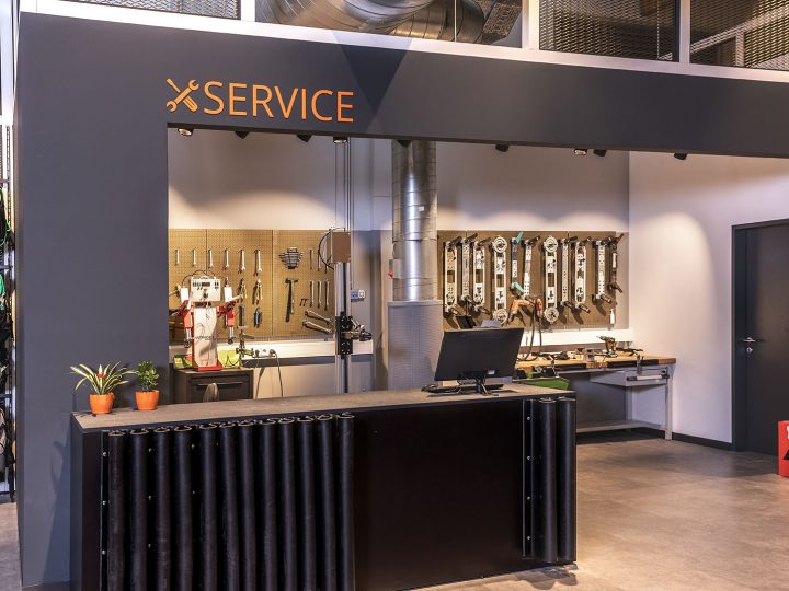 Tienda de servicio de esquí con mostrador en la parte delantera, herramientas montadas en la pared y una estación de trabajo en el fondo. A la izquierda, el equipo de esquí cuelga de los estantes. La palabra "SERVICIO" está estampada sobre el mostrador.