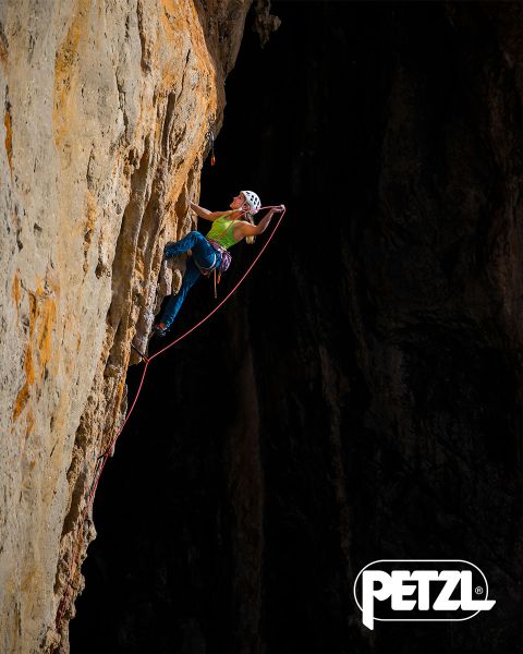 Un escalador con chaqueta verde y casco escala una formación de hielo masiva y colgante con piolets. Rocas cubiertas de nieve rodean el área. Arriba se muestran las palabras "Experimenta la diferencia" y el logo de Petzl.