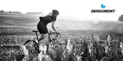 Un ciclista con casco conduce una bicicleta de carreras a través de un prado, con un paisaje montañoso al fondo. La imagen es en blanco y negro y el logotipo de Bergamont se puede ver en la esquina superior derecha.