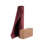 Eine teilweise gerollte rote Yogamatte steht aufrecht neben einem Yogablock aus Kork vor einem weißen Hintergrund.