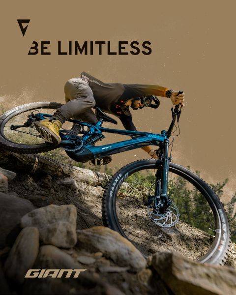Un ciclista conduce una bicicleta de montaña azul por terreno rocoso. Las palabras "Be Limitless" y "Giant" se ven en la imagen. El ciclista lleva casco y ropa de ciclismo, lo que subraya la aventura y la libertad en el sendero.