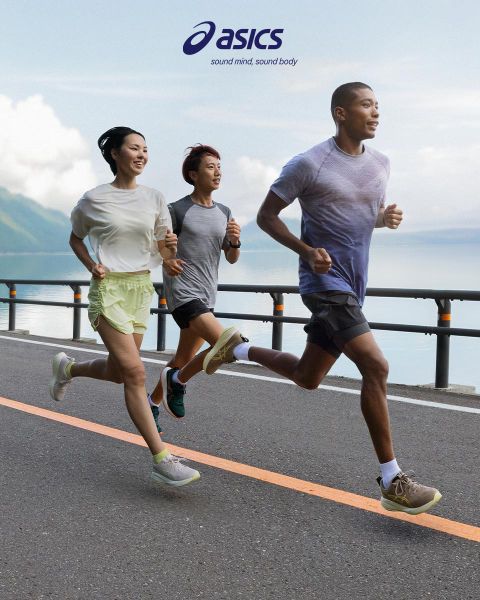 Tres personas corren en una calle junto a una gran masa de agua con montañas al fondo. El cielo está parcialmente nublado. Llevan ropa deportiva y parecen concentrados. El logotipo de ASICS y el eslogan están en la parte superior de la imagen.