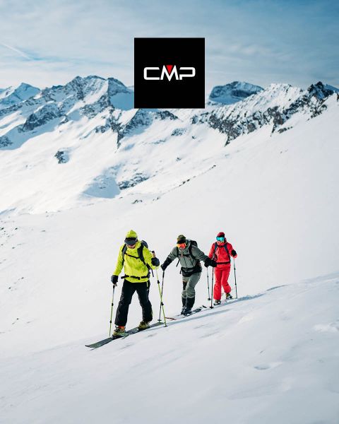 Tres esquiadores con atuendos coloridos ascienden a una montaña nevada bajo un cielo azul despejado, rodeados de altos picos nevados. El logo negro "CMP" aparece en la parte superior central de la imagen.