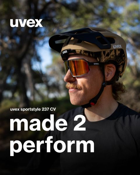 Una persona con bigote lleva unas gafas UVEX Sportstyle y un casco al aire libre. El texto dice: "UVEX sportstyle 237 CV made 2 perform". En el fondo se ven árboles y vegetación borrosa.