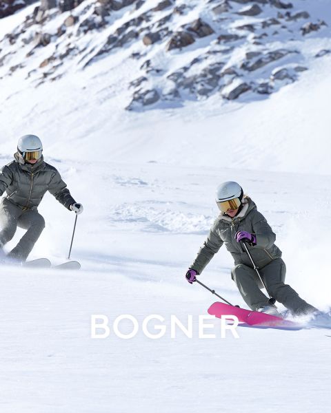 Dos esquiadores con equipo colorido. Izquierda: Persona de amarillo con gafas protectoras tirando de un trineo negro. Derecha: Dos personas con chaquetas amarillas y azules portando esquíes. Todos llevan cascos y gafas protectoras. Fondo nevado con "BOGNER" en el texto.