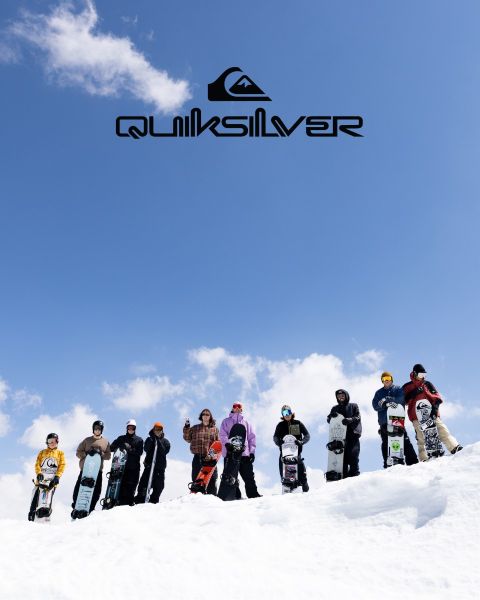 Un surfista cabalga una gran ola turquesa, personificando el equilibrio y la habilidad. Lleva pantalones cortos de baño oscuros, y la ola se encrespa sobre él. Encima de él se puede ver el logo de Quiksilver.