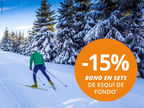 Una persona practicando esquí de fondo en una pista nevada, rodeada de pinos, con un gran círculo naranja que dice "-15% Bono en sets de esquí de fondo*".
