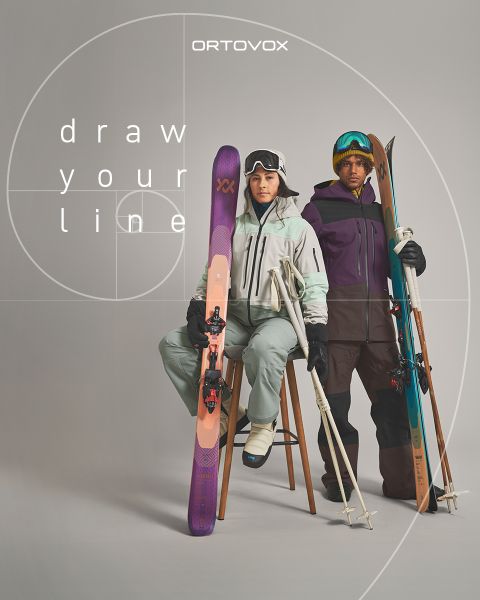 Tres personas con equipo para exteriores se sientan sonriendo y conversando en un terreno rocoso en una región montañosa. El sol se pone detrás de los picos. Una mochila y un termo están cerca. El logo de Ortovox está en la esquina superior derecha.