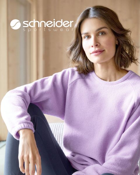 Una persona con cabello hasta los hombros, chaqueta informal y camiseta está de pie frente a un fondo neutro. En la parte superior de la imagen se puede ver la inscripción "Schneider Sportswear".