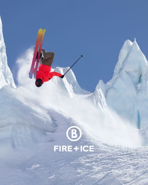 Dos personas con ropa de invierno esquían montaña arriba a través de la nieve. Llevan mochilas y usan bastones para apoyarse. En el fondo se ve un paisaje neblinoso y extenso. La imagen contiene un logo de "Fire + Ice" en la esquina superior izquierda.