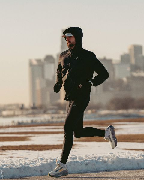 Una persona en ropa deportiva trota por un camino nevado en un día claro con el horizonte de la ciudad al fondo.
