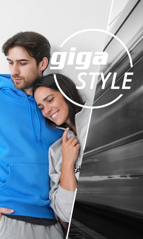 Una pareja sonriente en sudaderas con capucha se apoya a la izquierda contra una pared blanca, mientras que a la derecha aparece un tren borroso que se mueve rápidamente. El texto "giga STYLE" superpone la imagen.