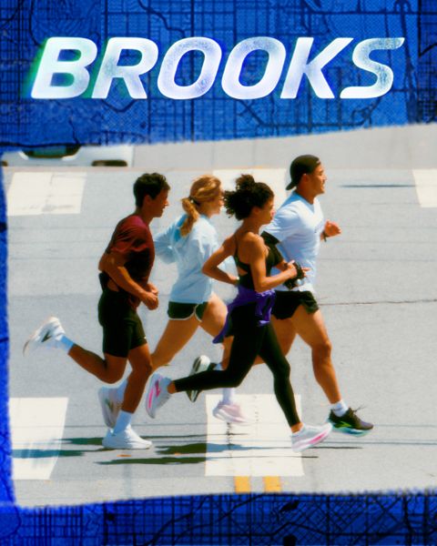 Un grupo de cinco personas corre enérgicamente por un paso de cebra. Llevan ropa deportiva colorida, incluyendo pantalones cortos y camisetas sin mangas. La escena es vibrante, con la palabra "BROOKS" estampada claramente encima de ellos.