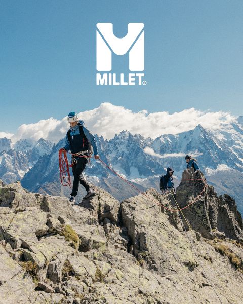 Tres excursionistas con todo el equipo caminan por un paisaje montañoso con picos nevados. Abajo se ve a una mujer con una chaqueta que se ajusta el cuello. Al fondo se ven montañas. Abajo a la derecha se ve el logo de "Millet".