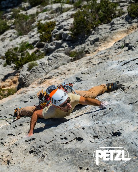 Un escalador con chaqueta verde y casco escala una formación de hielo masiva y colgante con piolets. Rocas cubiertas de nieve rodean el área. Arriba se muestran las palabras "Experimenta la diferencia" y el logo de Petzl.