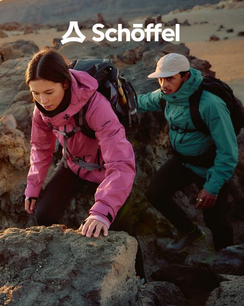 Dos personas con equipo para exteriores caminando sobre una colina cubierta de hierba con montañas y nubes al fondo. Encima de ellos está el logo de Schöffel, debajo una línea ondulada decorativa verde.