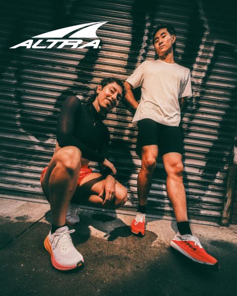 Dos personas posan con zapatillas de correr Altra delante de una puerta metálica cubierta de grafitis; encima de ellas aparece el logotipo de Altra.