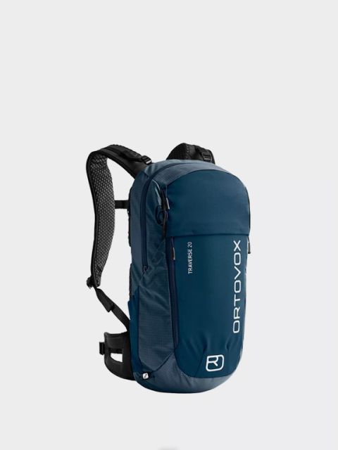 Mochila Ortovox azul con la palabra "Mochilas" encima. Con múltiples cremalleras, correas ajustables y detalles naranjas en los tiradores de las cremalleras y los clips. El nombre de la marca está impreso verticalmente en blanco.