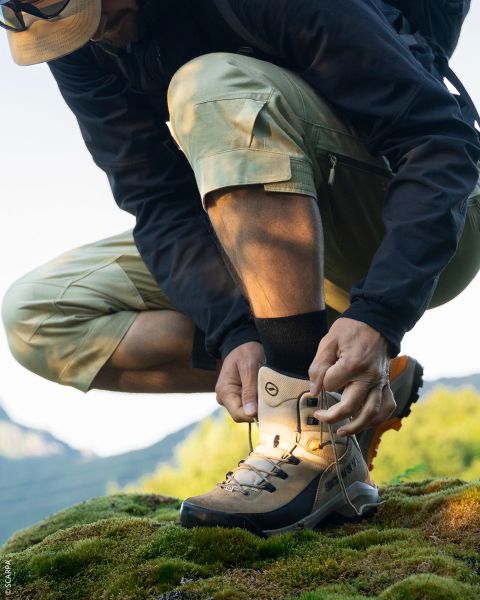 Primer plano de dos excursionistas de pie en un terreno rocoso, mirando sus zapatillas de trail La Sportiva bajo un cielo azul despejado.