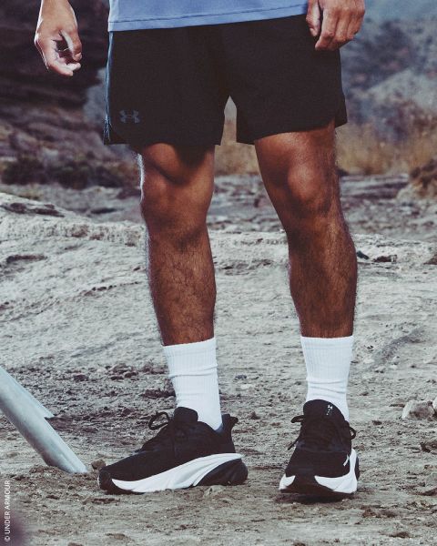 Una persona en shorts negros, calcetines blancos y zapatillas negras está de pie en un sendero rocoso al aire libre.