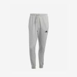 Hellgraue Adidas-Jogginghose mit umgeschlagenen Bündchen an den Knöcheln, Seitentaschen und einem schwarzen Adidas-Logo auf dem linken Oberschenkel, dargestellt vor einem schlichten weißen Hintergrund.