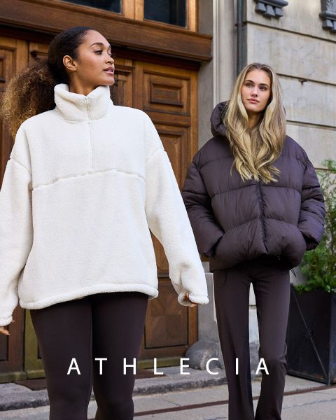 Dos mujeres vestidas con ropa deportiva azul de Athlecia posan en un terreno rocoso. Una lleva una sudadera y pantalones cortos, la otra un top corto blanco y pantalones azules. Encima de ellas se ve el nombre de la marca "Athlecia".