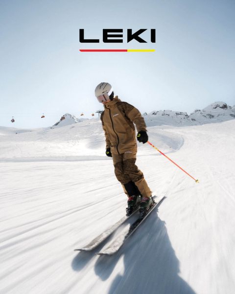 Un esquiador con chaqueta amarilla y gafas de esquí desciende una ladera nevada con bastones. En el fondo se ven montañas nevadas y un lago. El texto dice "¿CUÁL ES TU CAMPO DE JUEGO? SPITFIRE 3D" con un botón de "DESCUBRE AHORA".