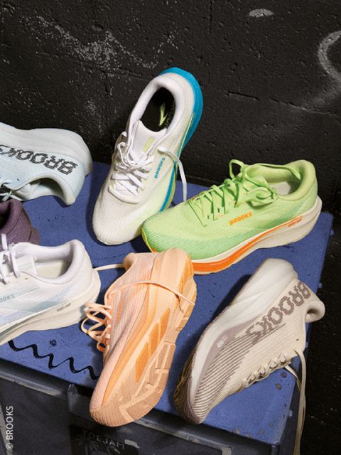 Una persona sostiene un par de zapatillas de correr de color blanco y rosa por los cordones sobre un zapatero de madera, junto a una sola zapatilla de correr de color negro y gris.