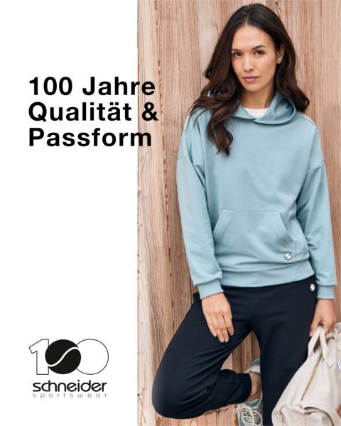 Una persona con cabello hasta los hombros, chaqueta informal y camiseta está de pie frente a un fondo neutro. En la parte superior de la imagen se puede ver la inscripción "Schneider Sportswear".