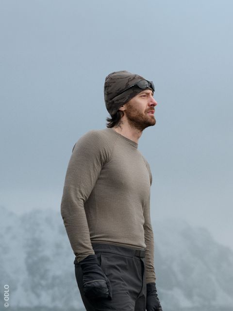 Un hombre y una mujer con ropa informal de invierno sentados al aire libre en un muro de piedra, sonriendo y conversando. Un par de esquíes están apoyados contra la pared y, al fondo, se ven montañas cubiertas de nieve.