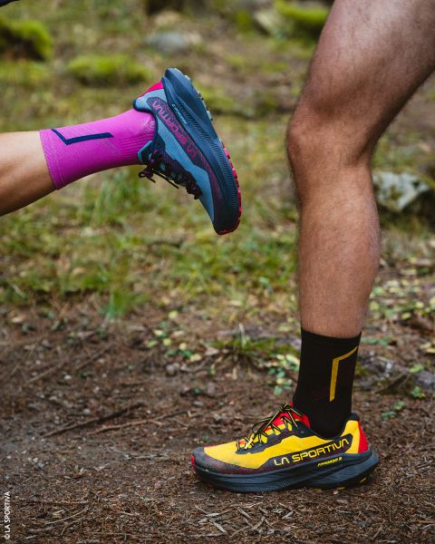 Dos piernas con zapatillas de trail running y calcetines deportivos, de pie en un camino de tierra.